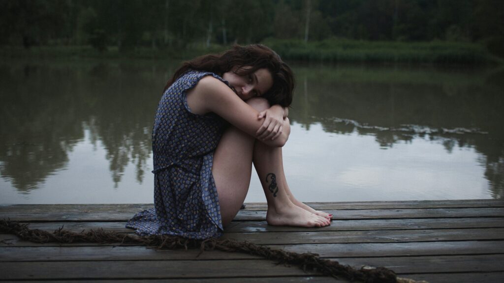 Woman sitting on a dock reflecting, representing perinatal grief and loss