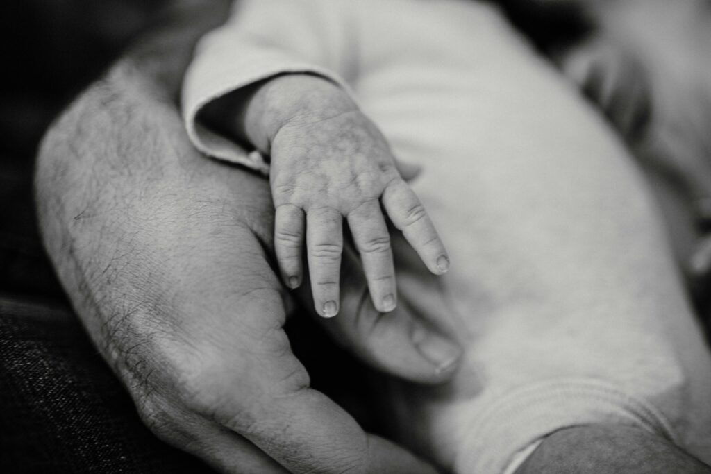 Tiny baby hand resting on father's hand, representing fatherhood and mental health in the perinatal period